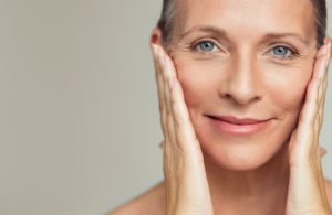 Mature woman smiling and touching her face, showing signs of ageing