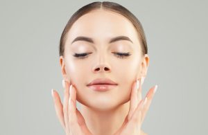 Woman with glowing skin and a defined V-shaped face touching her cheeks gently.